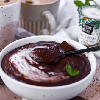 Schokoladenpudding mit Kaffeetassen und Kochcreme im Hintergrund