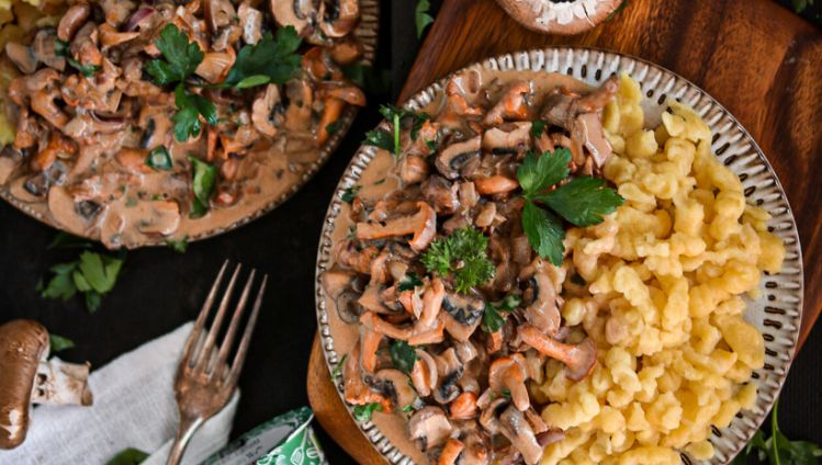 Pilzsauce mit Spätzle auf Tellern auf Holzbrett und rundherum dekoriert