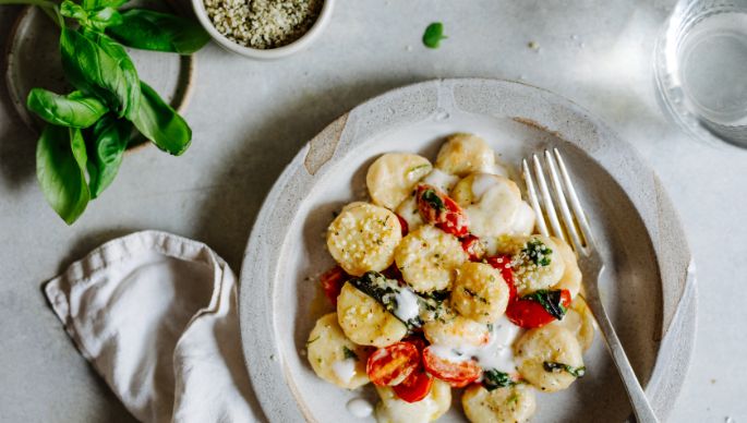 Gnocchi mit Kräutersauce, Basilikum, Tomaten und Hanfsamen auf Teller gedeckt und rundherum dekoriert