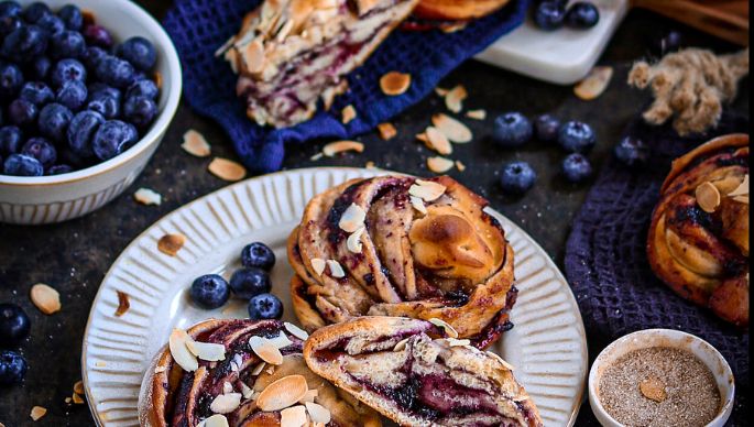 Zimt-Blaubeer-Knoten mit mehreren Zimt-Blaubeer-Knoten im Hintergrund und Heidelbeeren und Kaffee