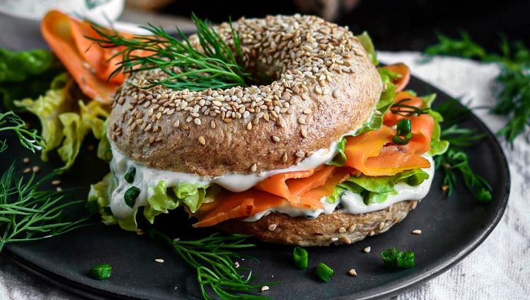 Bagel mit Creme, Karottenlachs und Salat auf Teller