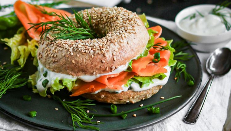 Bagel gefüllt mit Karottenlachs, Salat und Creme auf Teller