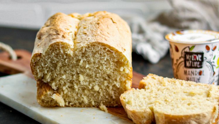 angeschnittenes weißes Joghurtbrot auf Brett mit Mandel-Joghurtalternative Natur im Hintergrund