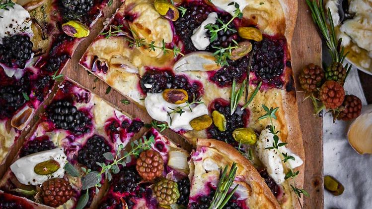 eckiger Flammkuchen mit Brombeeren, Creme und Gewürzen auf Holzbrett dekoriert