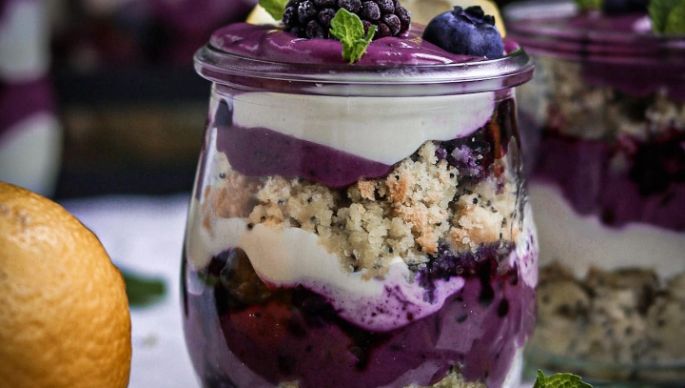 Zitronen-Mohnkuchen mit Beerencreme und weißer Creme geschichtet in Glas mit Dekoration