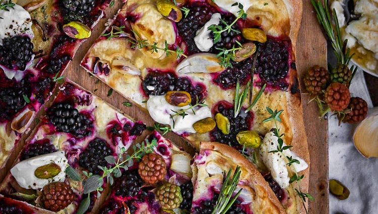 eckiger Flammkuchen mit Brombeeren, Creme und Gewürzen auf Holzbrett dekoriert